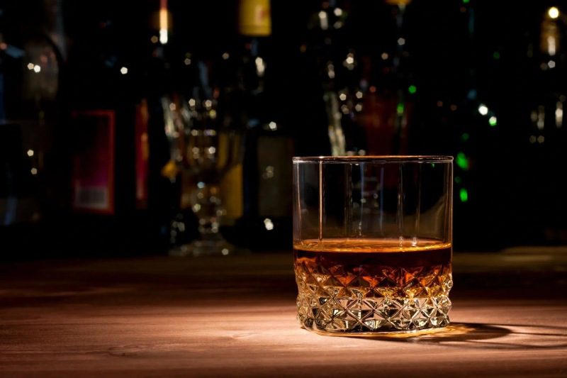 Glass of Whiskey on Wood With Bottles